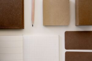 Top view of minimalist brown and white stationery items, including a notebook and pencil, arranged neatly.